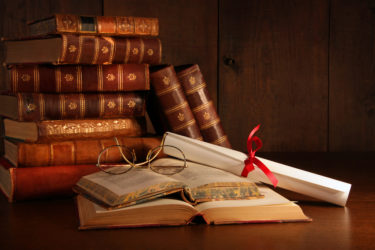 Pile of old books with reading glasses on desk