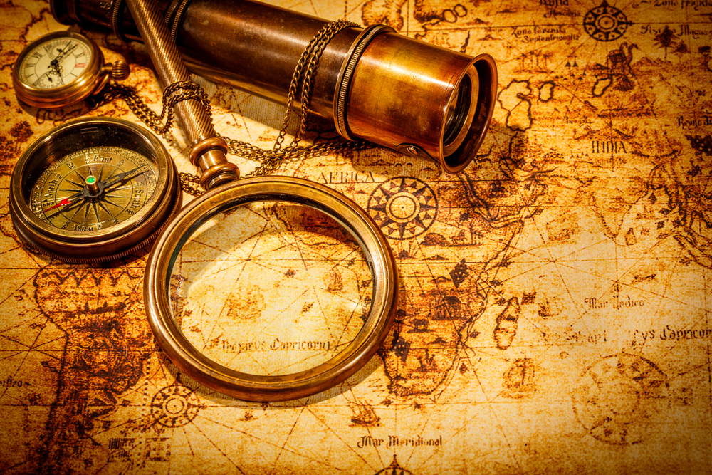 Vintage magnifying glass, compass, telescope and a pocket watch lying on an old map.