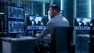 Technical Controller Working at His Workstation with Multiple Displays. Displays Show Various Technical Information. He's Alone in System Control Center.