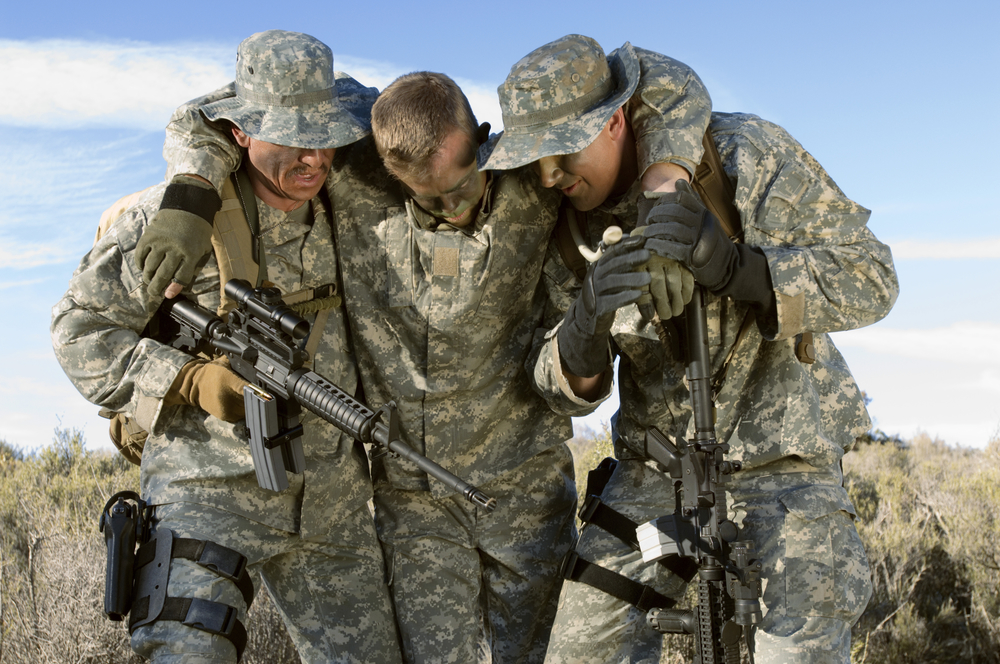 Soldiers walking in field carrying colleague